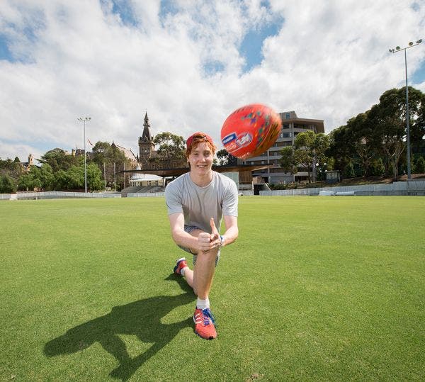 Male AFL player handballing the ball towards the camera