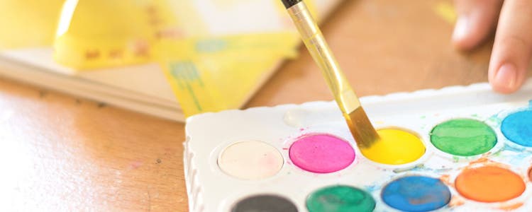 Vibrant watercolour palette with paintbrush dipping in yellow.
