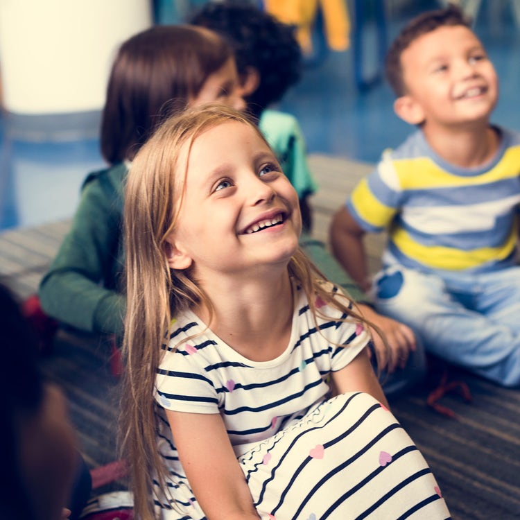 Preschoolers sitting on the floor in a classroom smiling up