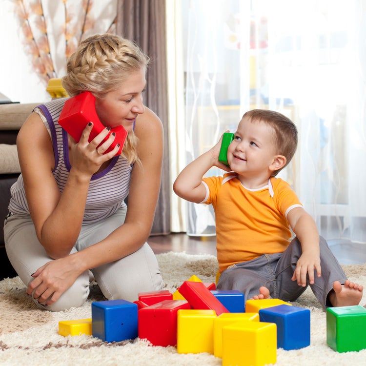 Teacher playing pretend with child, using bricks as telephones