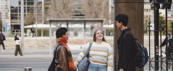 Three students standing by a tram stop outside the university