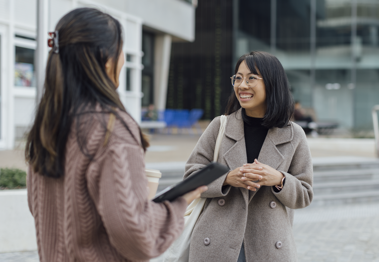 Two students talk smiling outdoors.