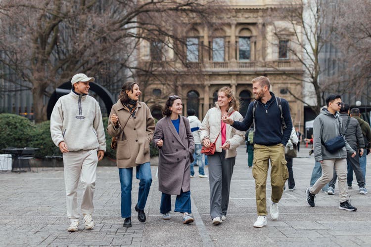 5 students talking as they walk towards the camera in front of a heritage University building