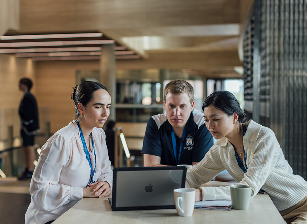 Three people seated and looking at a laptop screen