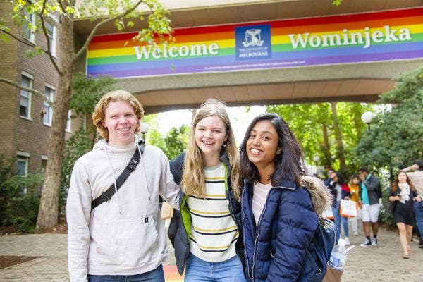 3 students pose for a photo outside of the Welcome sign which is coloured in rainbow in support of Pride Month