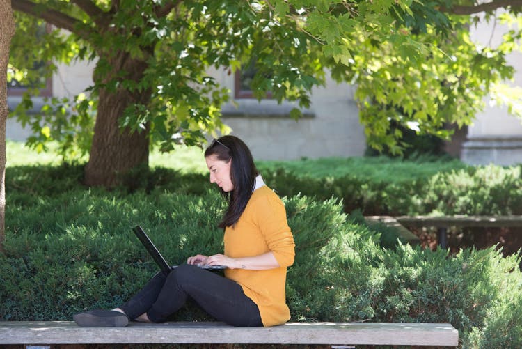 Student studying on park bench with laptop
