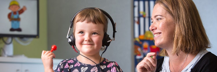 young child with headphones on and woman smiling