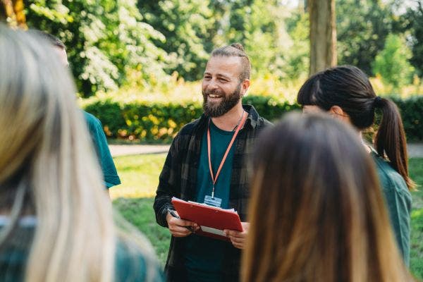 A male social worker talking to a group of people in a park.