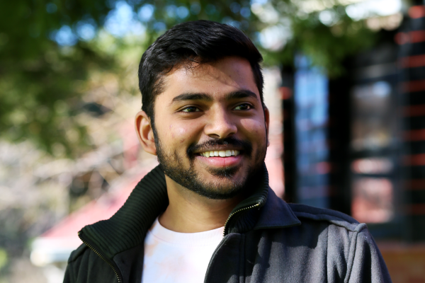Nirmalsinh stands outside under a tree smiling to the right of camera.