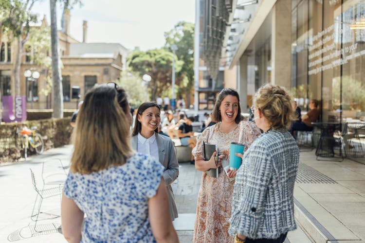 A group of happy women are standing outside of a cafe on campus and talking