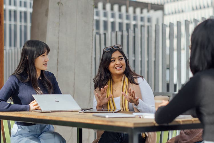 Three mature-age female students sitting outdoors and discussing a project