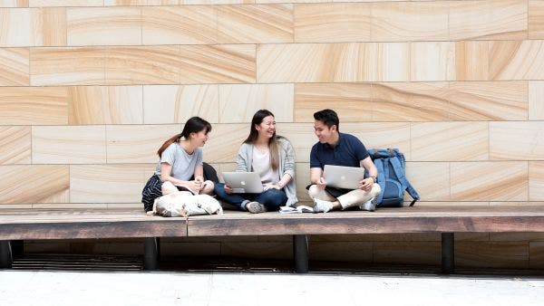 Three students with laptops on campus