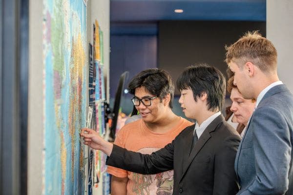 Monishi stands with three students putting pins on a world map