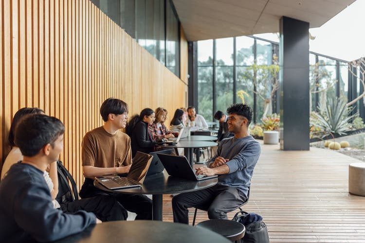 A group of students sitting on a balcony with laptops open