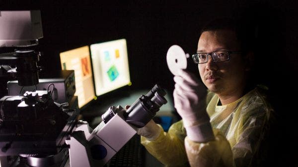 A researcher sitting next to a microscope in a dark room